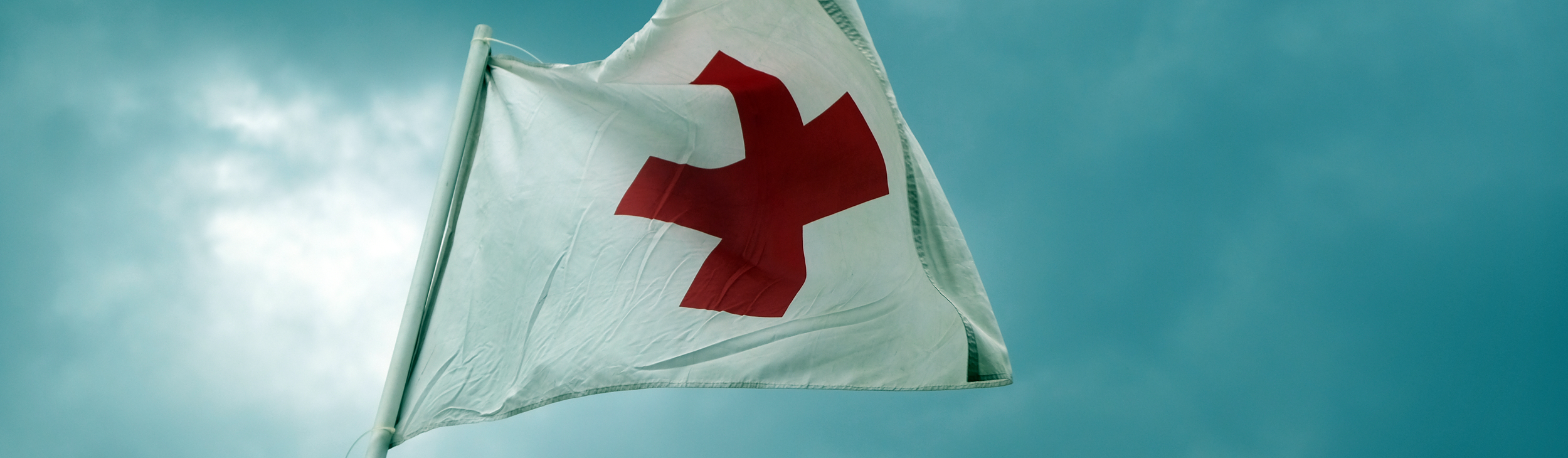 flas Image of white first aid flag with Red Cross logo, against a cloudy blue sky